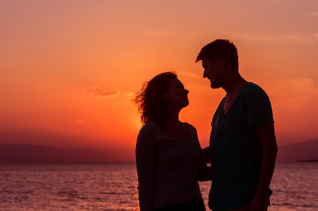 Casal jovem curtindo o pôr do sol em pé na praia