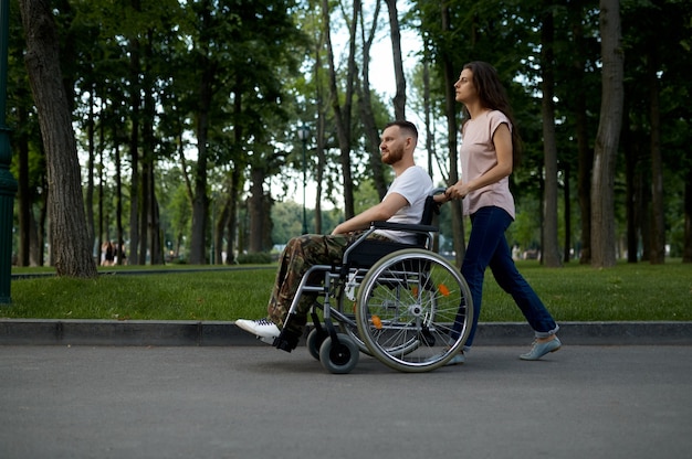 Casal jovem da família com cadeira de rodas, caminhando no parque. veterano paralítico e com deficiência, cuidar de um homem deficiente. marido e mulher superam dificuldades juntos, relacionamentos afetuosos