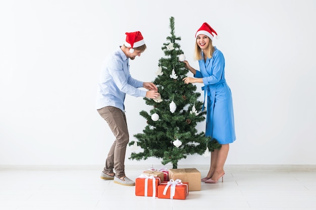 Casal jovem da família com chapéu de papai noel decorando a árvore de natal