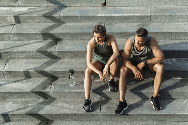 Casal jovem de atletas sentados na escada de concreto depois de correr ou fazer exercícios físicos ao ar livre