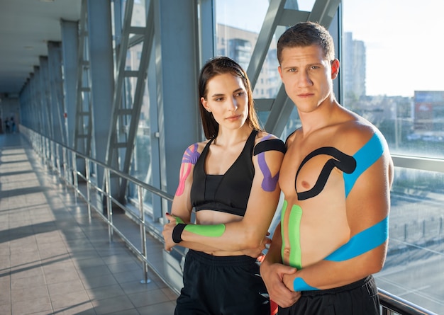 Casal jovem de esportes com fita cinesiológica posando dentro de casa.