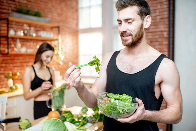 Casal jovem de esportes fazendo um lanche com salada saudável e suco verde na cozinha em casa