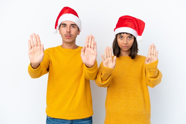 Casal jovem de raça mista comemorando o Natal isolado no fundo branco fazendo gesto de parada para decepcionado com uma opinião