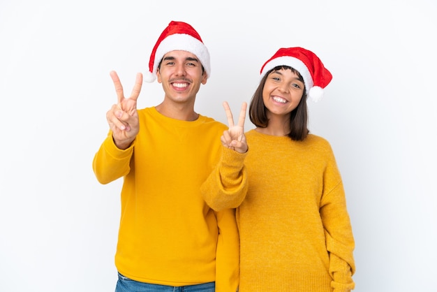 Casal jovem de raça mista comemorando o Natal isolado no fundo branco sorrindo e mostrando sinal de vitória