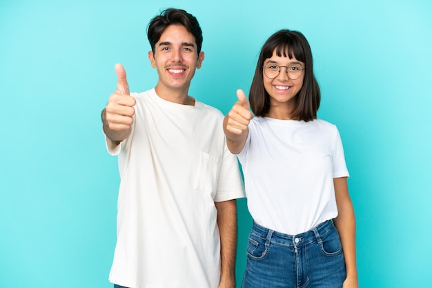 Casal jovem de raça mista isolado em fundo azul dando um polegar para cima gesto porque algo de bom aconteceu