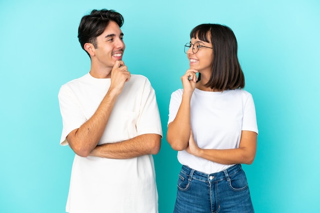 Casal jovem de raça mista isolado em fundo azul olhando um para o outro