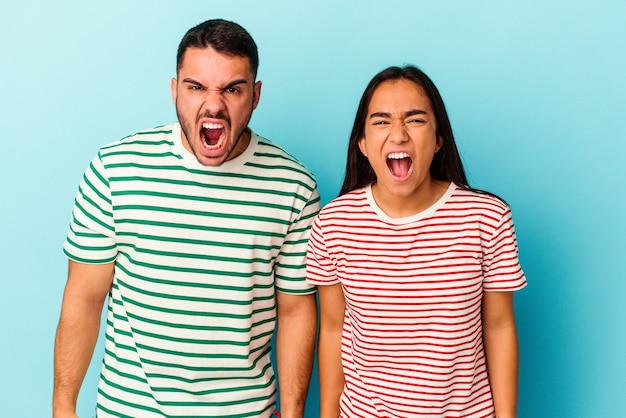 Casal jovem de raça mista isolado no azul, gritando muito zangado e agressivo.