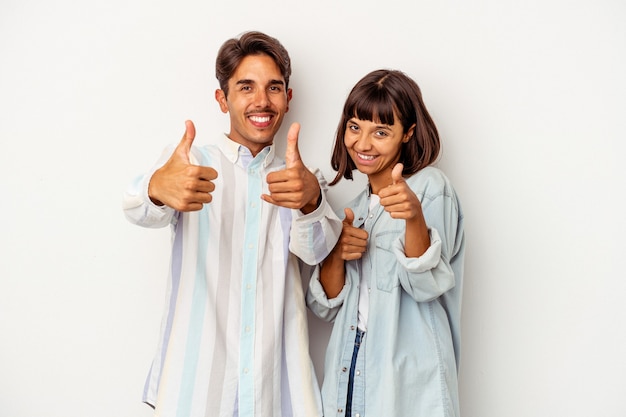 Casal jovem de raça mista, isolado no fundo branco, levantando os dois polegares, sorrindo e confiante.