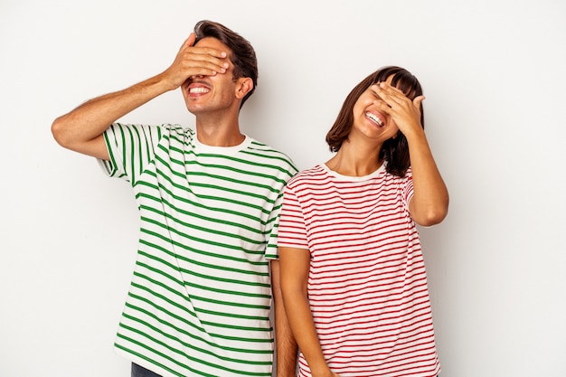 Casal jovem de raça mista, isolado no fundo branco, ri, mantendo as mãos na cabeça com alegria. Conceito de felicidade.