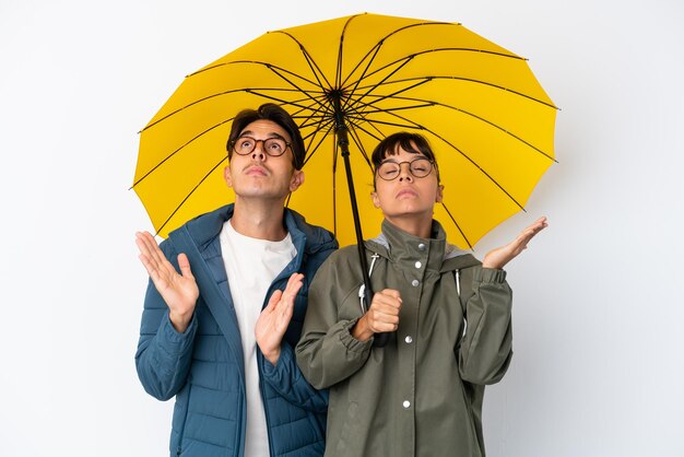 Casal jovem de raça mista segurando um guarda-chuva isolado no fundo branco frustrado por uma situação ruim