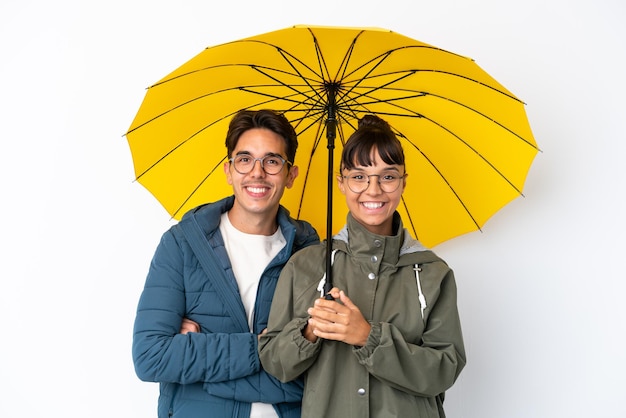 Casal jovem de raça mista segurando um guarda-chuva isolado no fundo branco, mantendo os braços cruzados em posição frontal