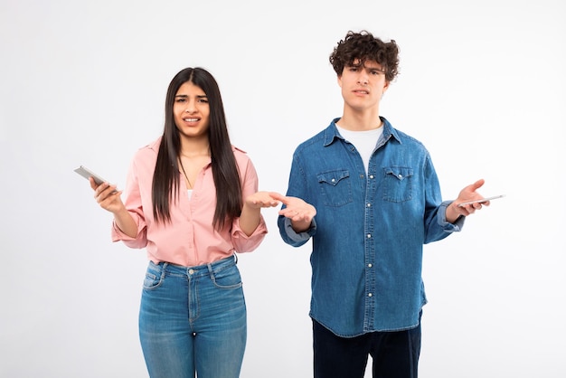 Casal jovem descontente segurando telefones celulares sobre fundo de estúdio branco