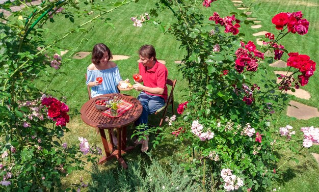 Casal jovem desfrutando de comida e bebidas no lindo jardim de rosas na vista aérea de encontro romântico