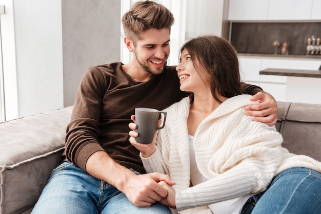 Casal jovem e adorável sentado e bebendo café no sofá em casa