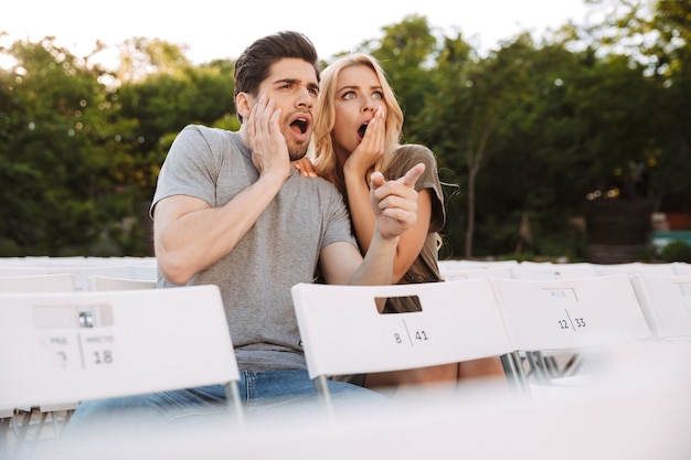 Casal jovem e adorável sentado em cadeiras e assistindo a um filme ao ar livre