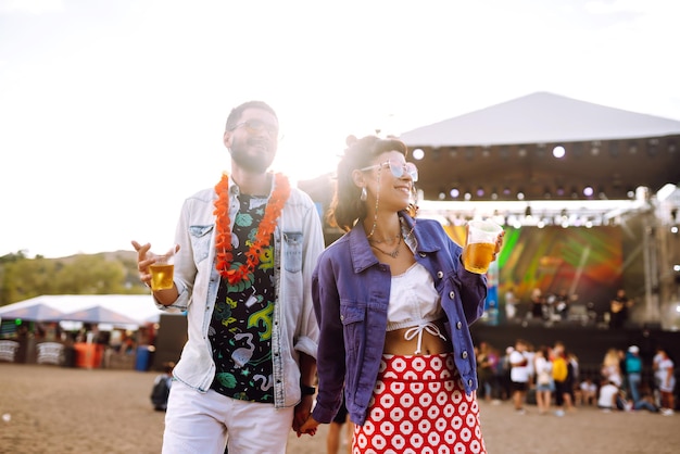 Foto casal jovem e alegre no festival de música amigos felizes bebendo cerveja e se divertindo