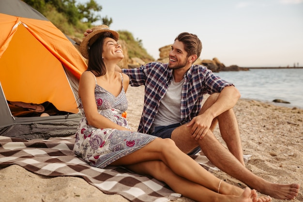 Casal jovem e alegre se divertindo acampando na praia