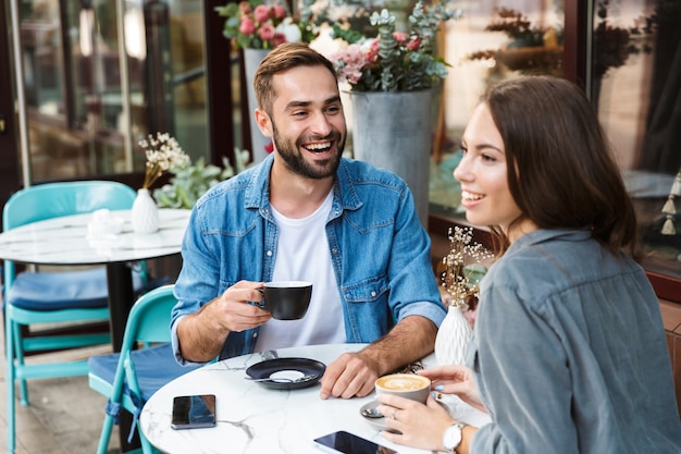 Casal jovem e atraente apaixonado almoçando enquanto está sentado à mesa do café ao ar livre, bebendo café, conversando