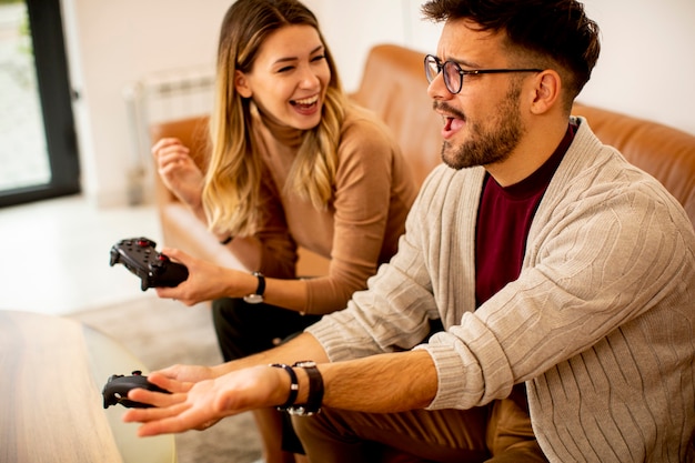 Casal jovem e bonito jogando videogame em casa, sentado no sofá e se divertindo