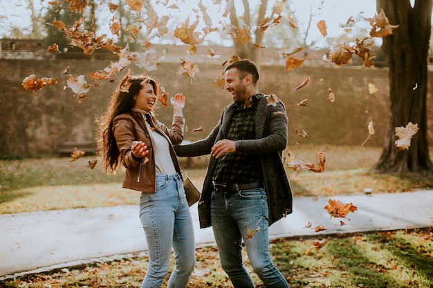 Casal jovem e bonito se divertindo com folhas no parque outono