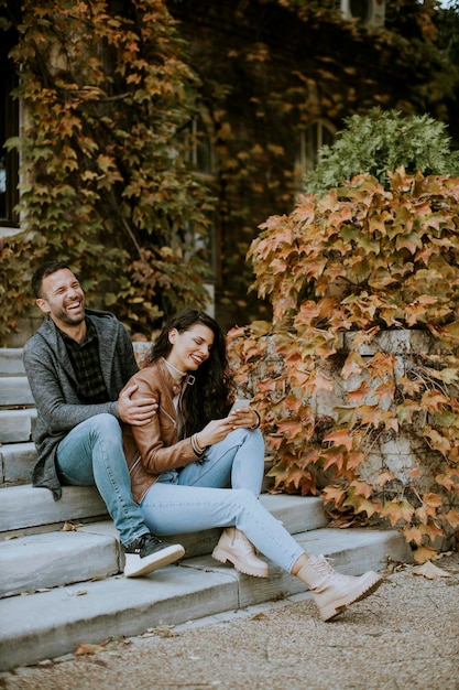 Foto casal jovem e bonito sentado em uma escada externa em um dia de outono e usando um telefone celular