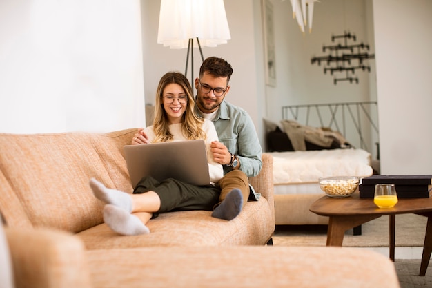 Foto casal jovem e bonito usando laptop enquanto está sentado no sofá em casa