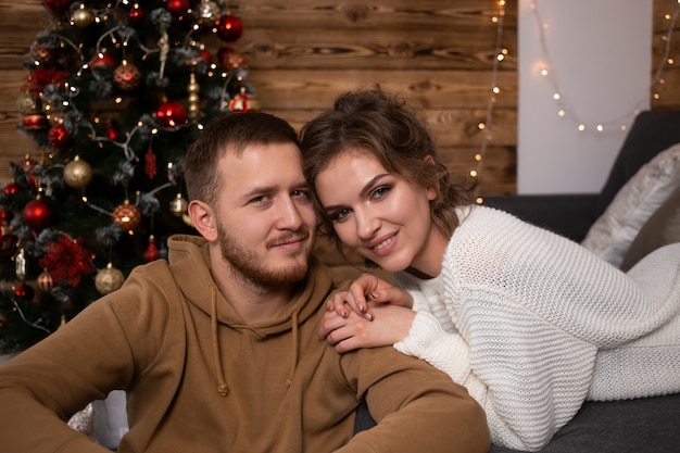 Casal jovem em casa na época do natal, perto de uma árvore de natal lindamente decorada