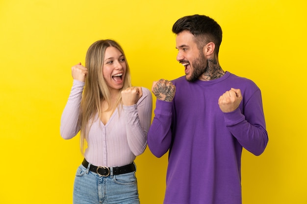 Casal jovem em fundo amarelo isolado comemorando vitória