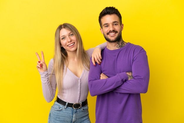 Casal jovem em fundo amarelo isolado sorrindo e mostrando sinal de vitória