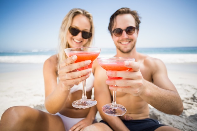 Casal jovem em óculos de sol, mostrando o copo de cocktail na praia