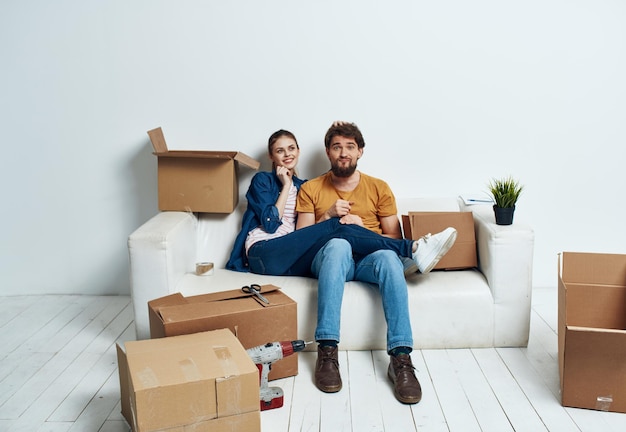 Casal jovem em um novo apartamento em caixas de sofá branco com coisas se movendo