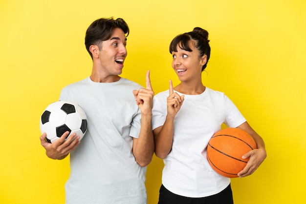 Casal jovem esportivo jogando futebol e basquete isolado em fundo amarelo com a intenção de perceber a solução enquanto levanta um dedo