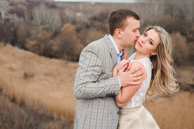 Casal jovem feliz abraçando na beira da montanha, no fundo uma paisagem muito bonita.