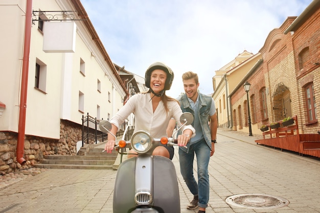 Casal jovem feliz andando de scooter na cidade. um cara bonito e uma jovem mulher viajam. conceito de aventura e férias.