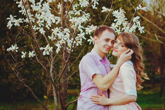 Casal jovem feliz andando no parque primavera. Luz do pôr do sol. Flores de magnólia florescendo. Ame. Encontro. Beijo