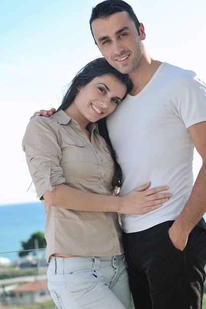 casal jovem feliz apaixonado tem romance relaxa na varanda ao ar livre com oceano e céu azul ao fundo