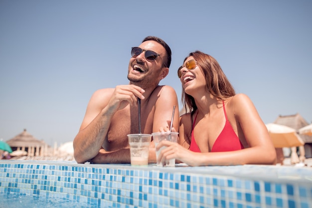 Casal jovem feliz bebendo um coquetel na piscina