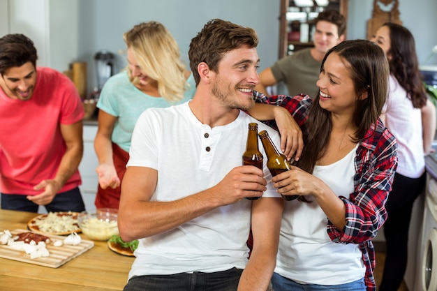 Foto casal jovem feliz, brindando a garrafas de cerveja em casa