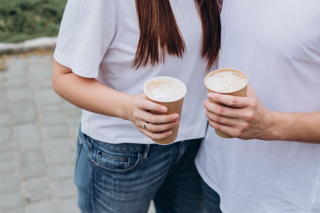 Casal jovem feliz caminha pelas ruas da cidade e bebe café de um copo de papelão.