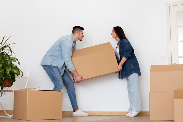 Casal jovem feliz carregando uma grande caixa de papelão com pertences em casa