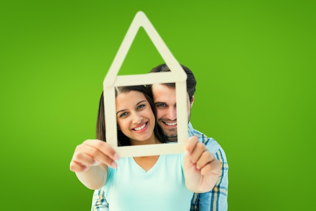 Foto casal jovem feliz com forma de casa contra vinheta verde