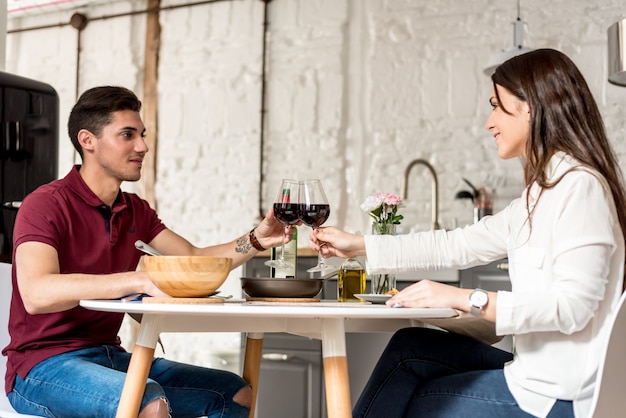 Casal jovem feliz comendo e bebendo vinho em casa