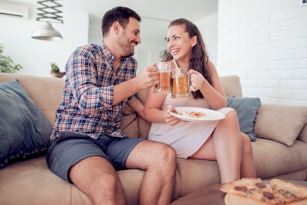 Casal jovem feliz comendo pizza na sala de estar