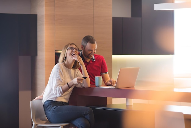 casal jovem feliz comprando on-line usando laptop, computador e cartão de crédito em sua casa de luxo