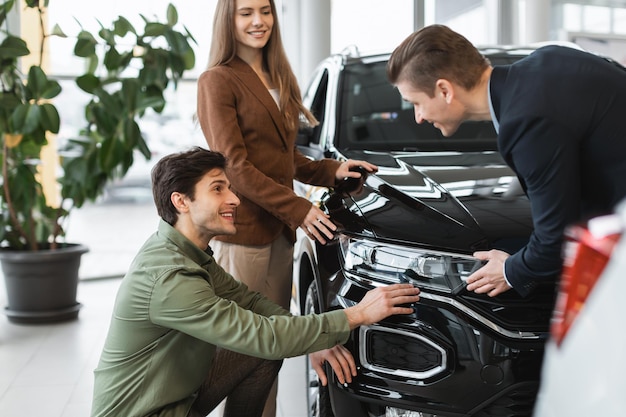 Foto casal jovem feliz consultando vendedor selecionando carro novo na loja de concessionárias de automóveis