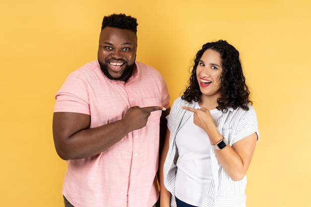 Foto casal jovem feliz em roupas casuais juntos apontando dedos olhando sorrindo para a câmera