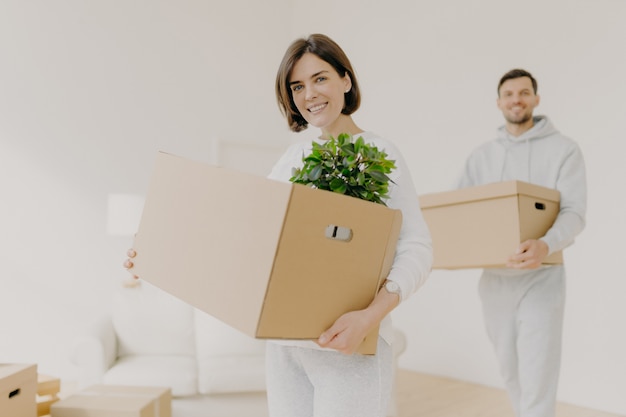 Casal jovem feliz entra própria casa moderna, compra imóveis, carrega caixas de papelão com planta interna