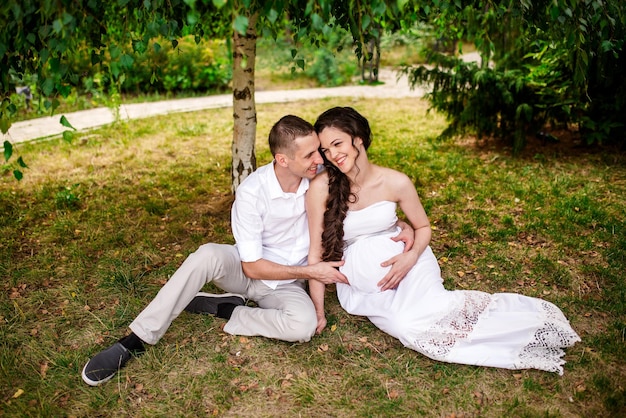 Casal jovem feliz esperando bebê mulher grávida com marido tocando a barriga sentado na grama verde