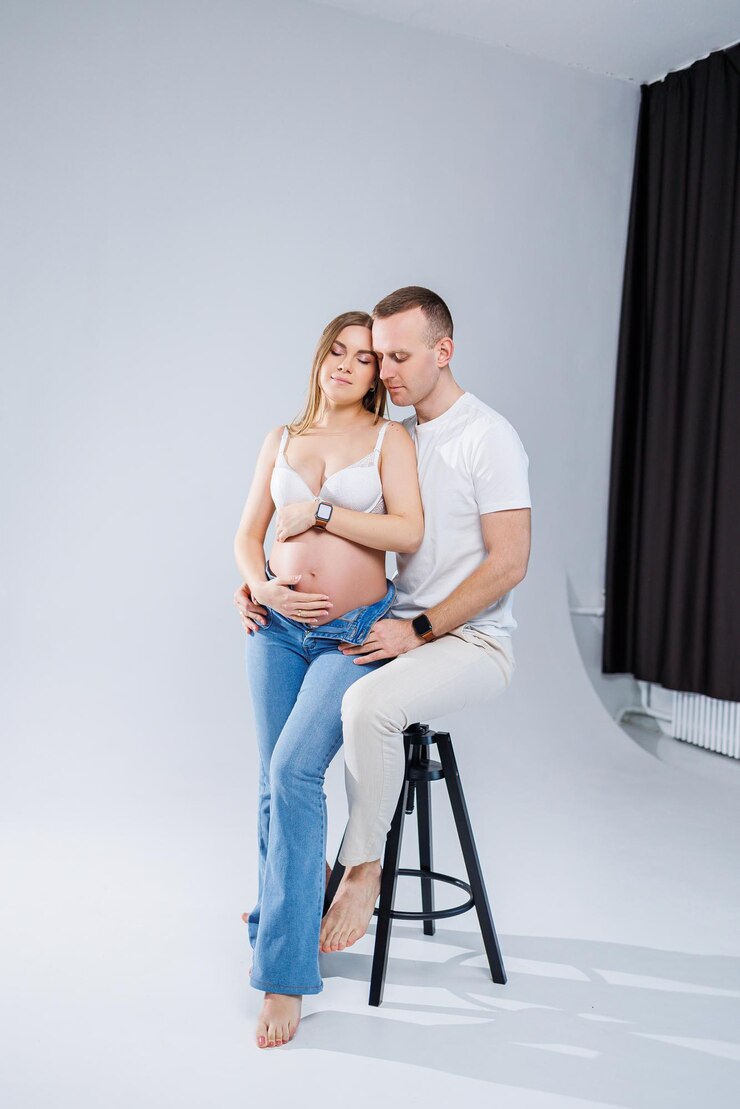 Foto casal jovem feliz esperando um bebê em camisetas brancas e jeans em um fundo branco felicidade da gravidez e do parto um casal feliz está esperando um filho