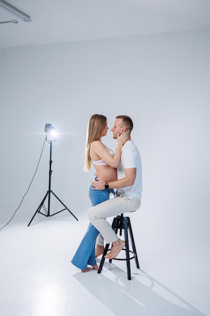 Casal jovem feliz esperando um bebê em camisetas brancas e jeans em um fundo branco felicidade da gravidez e do parto Um casal feliz está esperando um filho